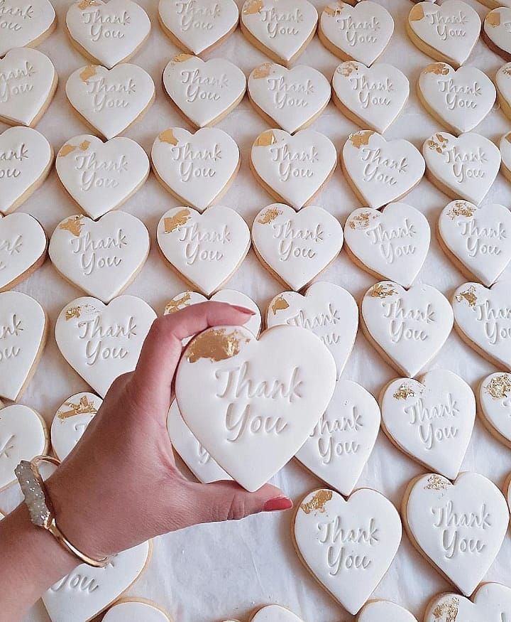 a hand holding a heart shaped cookie with the words thank you written on it in gold foil