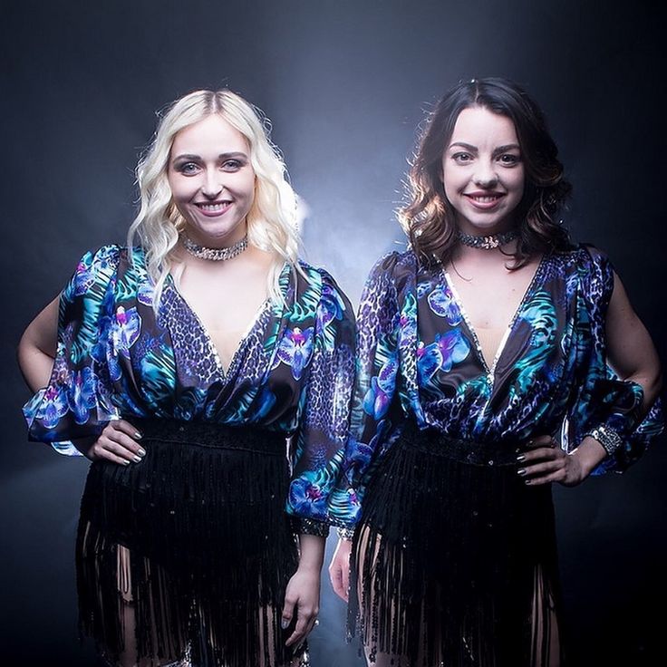 two women standing next to each other in front of a black background wearing fringe skirts