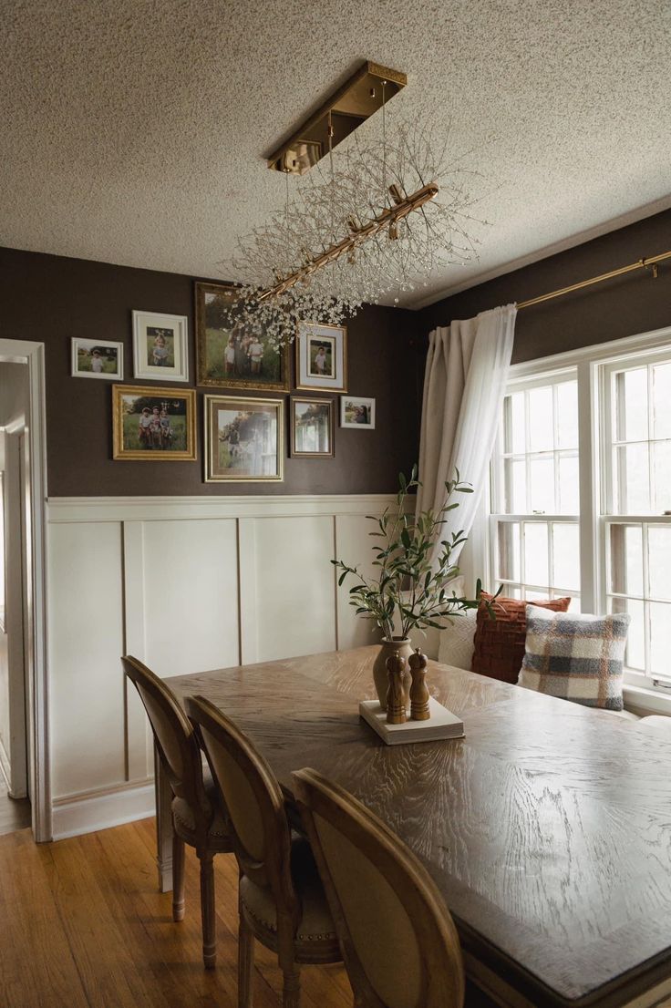 a dining room table with chairs and pictures on the wall above it, in front of a window