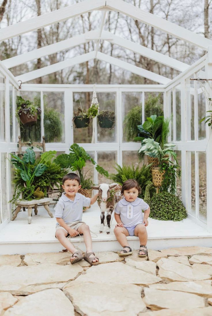 two young boys sitting next to each other in front of a greenhouse