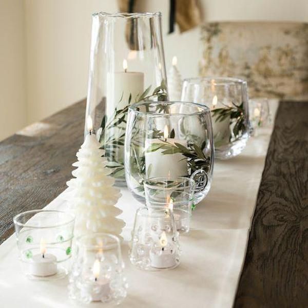 a table topped with candles and glass vases filled with greenery on top of a wooden table