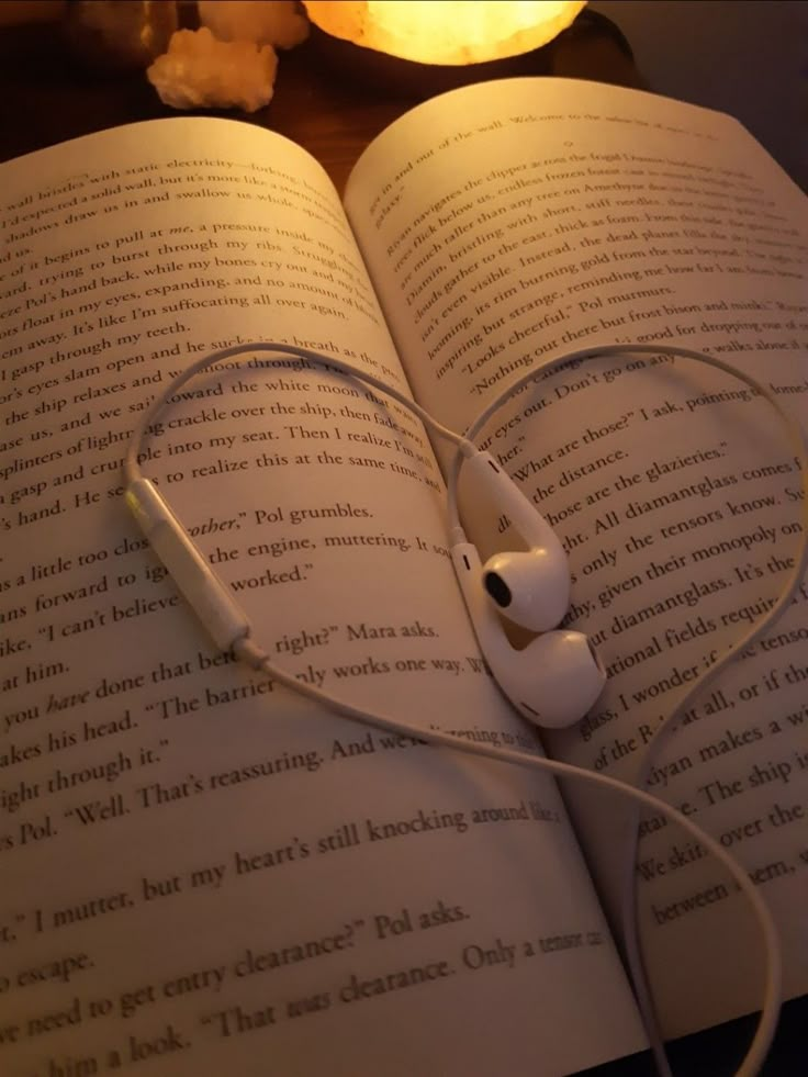 an open book with headphones on top of it and a lit candle in the background