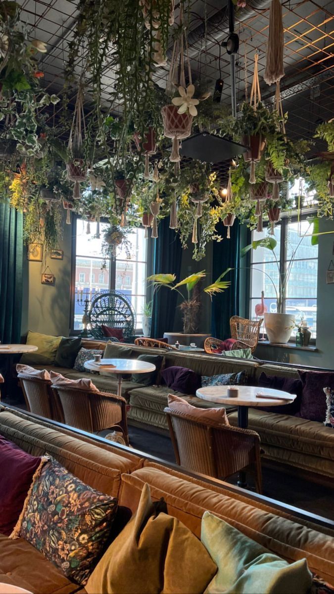 the interior of a restaurant with plants hanging from the ceiling and couches on either side