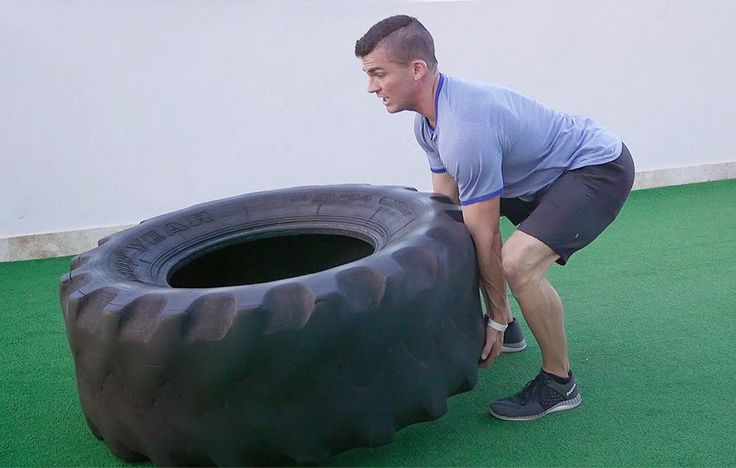 a man pushing a large tire on the ground