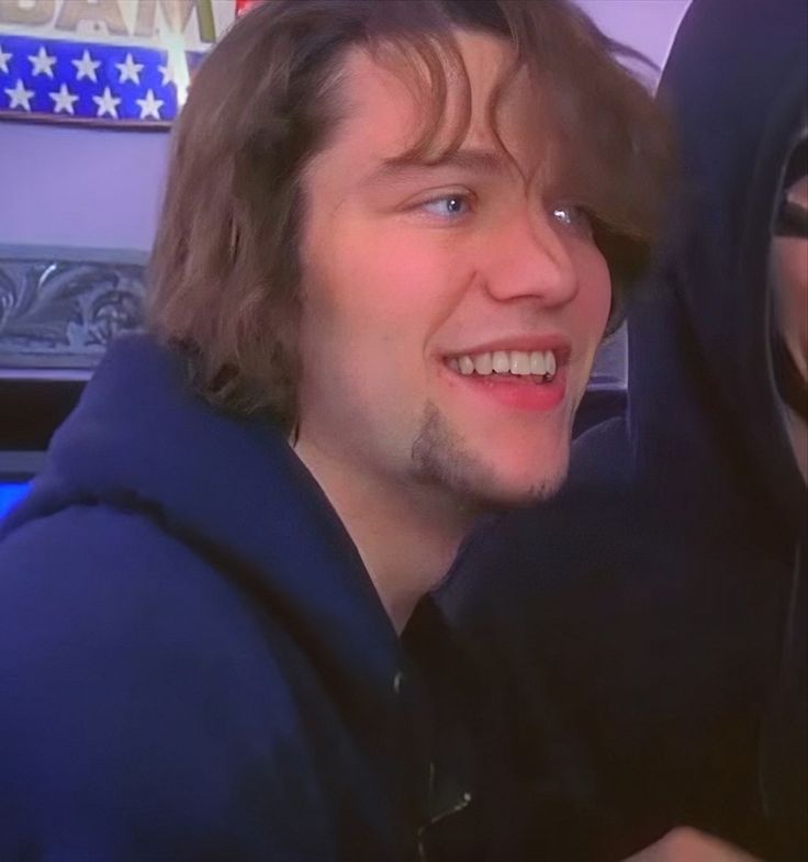 a man in a blue hoodie is smiling and looking at the camera with another person behind him