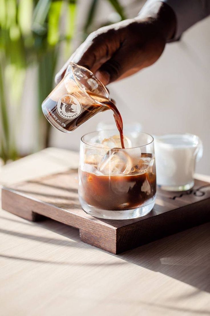 a person pours coffee into a glass on a tray with two cups next to it