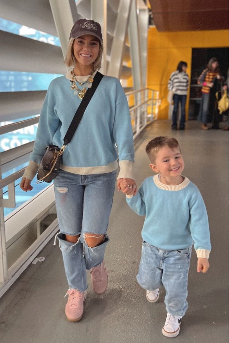 a woman holding the hand of a small boy who is wearing ripped jeans and a blue sweater