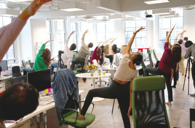 a group of people doing yoga exercises in an office setting with their arms raised up