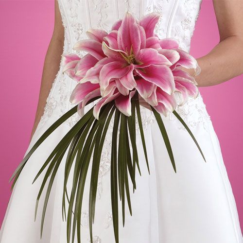 a woman in a white dress holding a bouquet of pink flowers and palm fronds