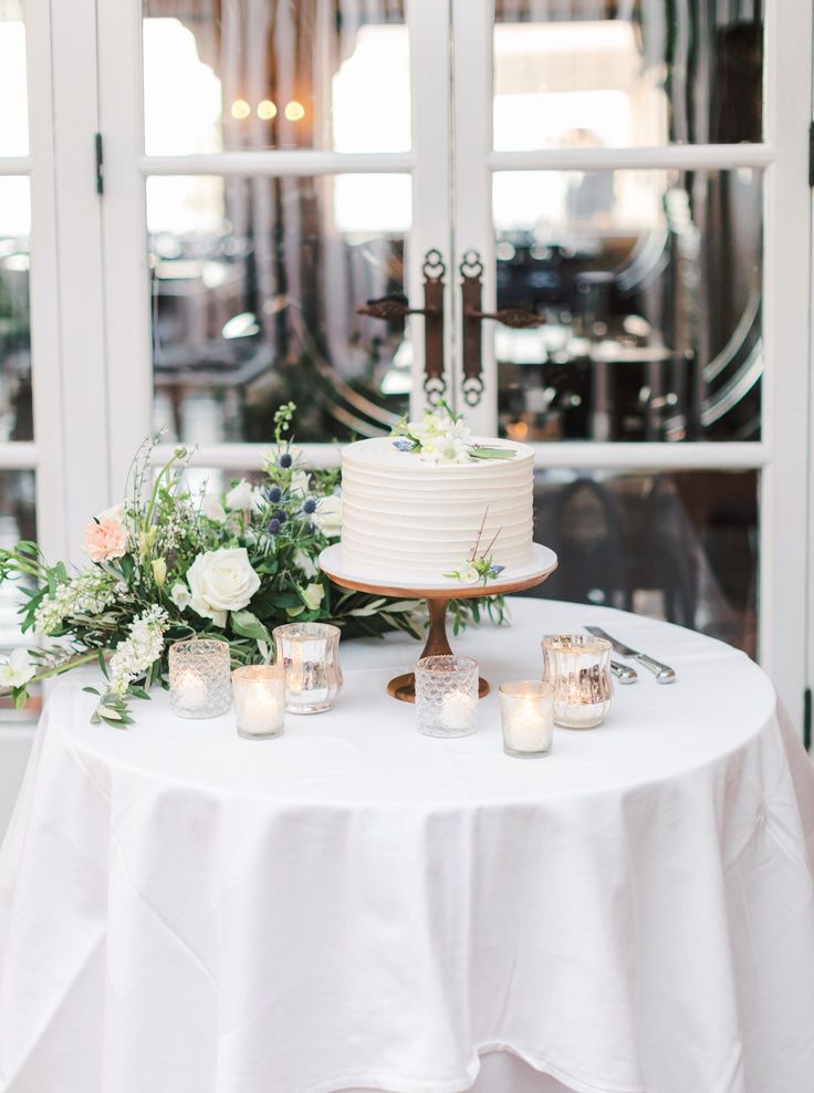 a table with a cake and candles on it in front of a window at a wedding