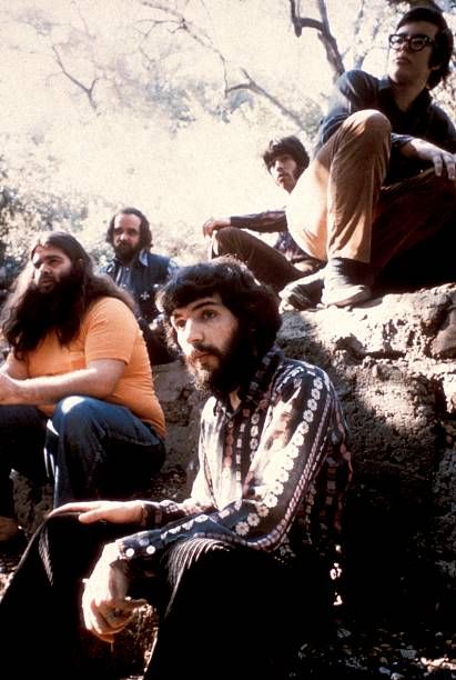 a group of men sitting next to each other on top of a rocky hillside with trees in the background