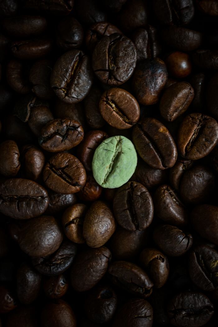 a green piece of food sitting on top of some coffee beans in the middle of a pile