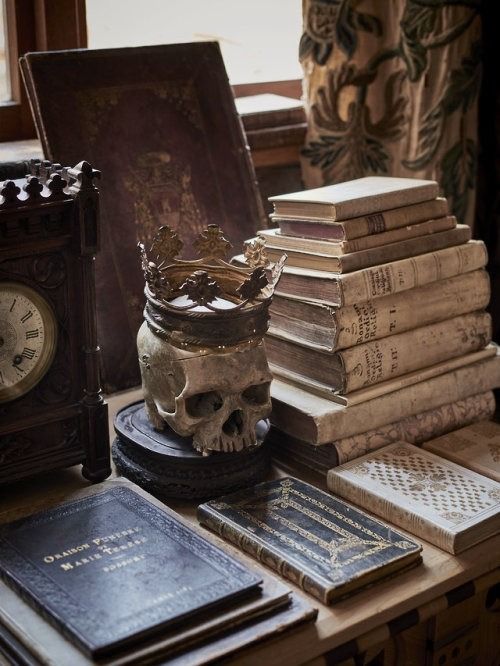 there are many books on the table with a skull statue next to it and a clock