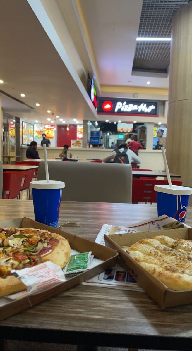 two pizzas are sitting on the table in front of some people at a fast food restaurant