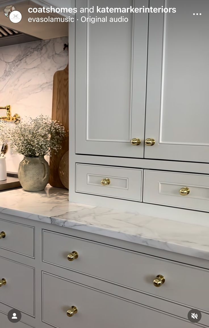 a kitchen with white cabinets and marble counter tops, gold pulls on the handles in front of an oven