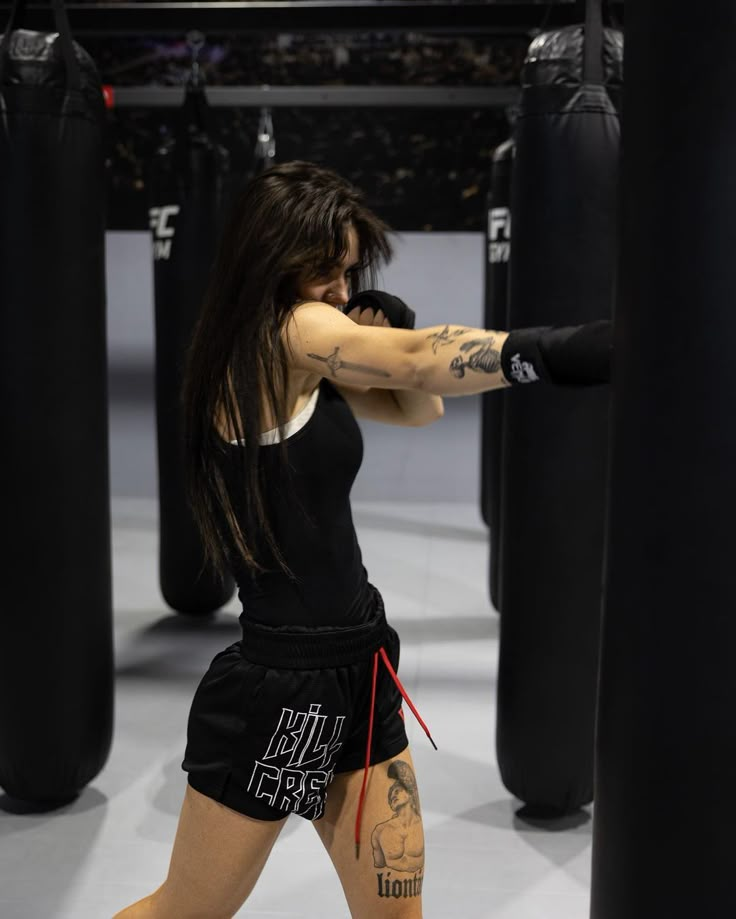 a woman with tattoos on her arms and legs is boxing in a gym ring while wearing black shorts