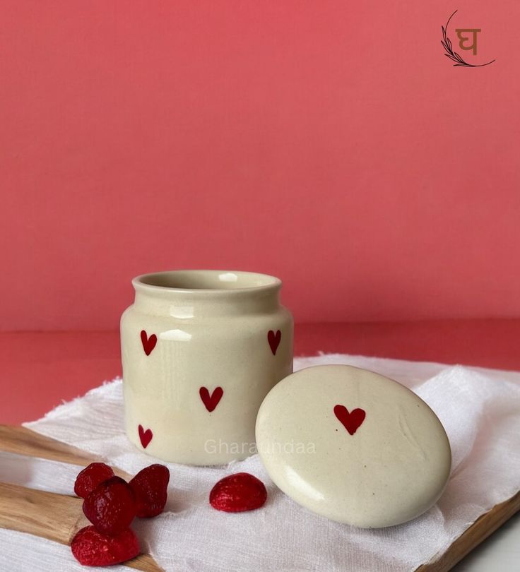 two white jars with hearts painted on them next to some spoons and strawberries