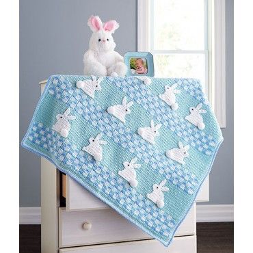 a white stuffed rabbit sitting on top of a bed next to a baby's blanket