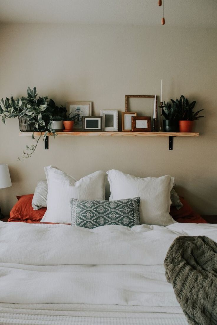 a bed with white sheets, pillows and plants on the shelves above it in a bedroom