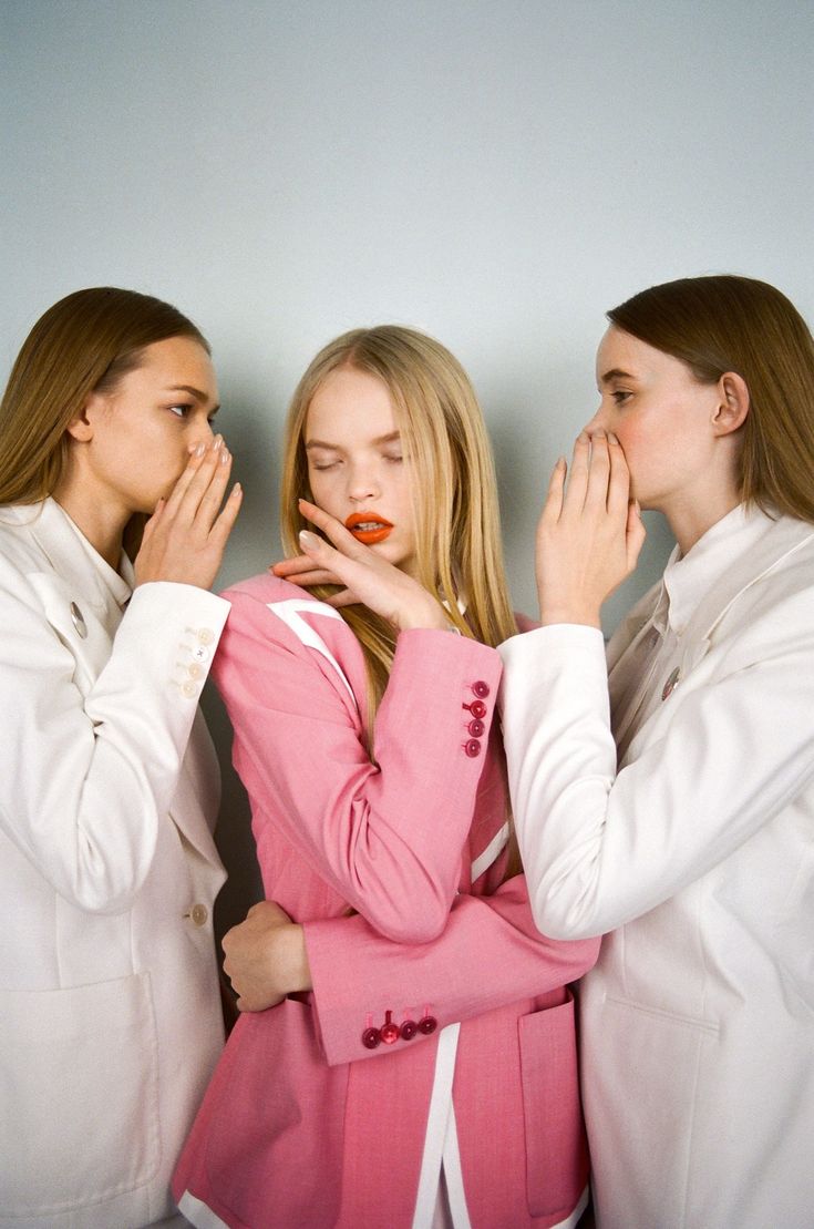 three women standing next to each other in front of a white wall with their hands on their mouths