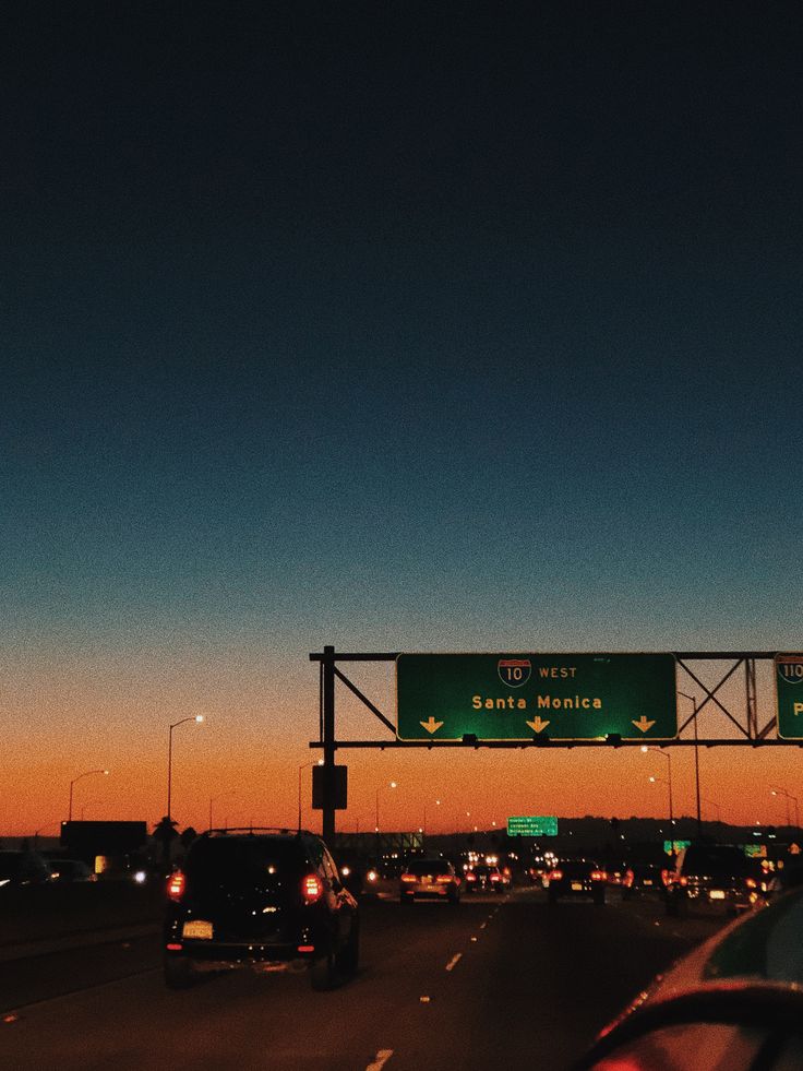 an exit sign on the side of a highway at dusk with traffic going by in the distance