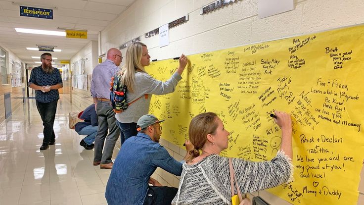 several people writing on a yellow board in a hallway