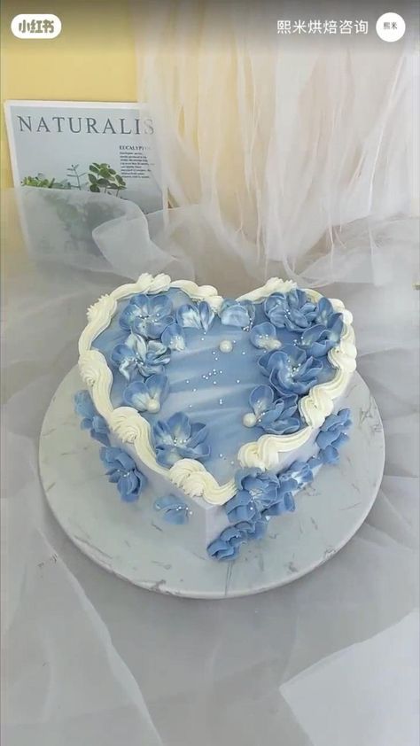 a heart shaped cake with blue flowers on it and a book in the back ground