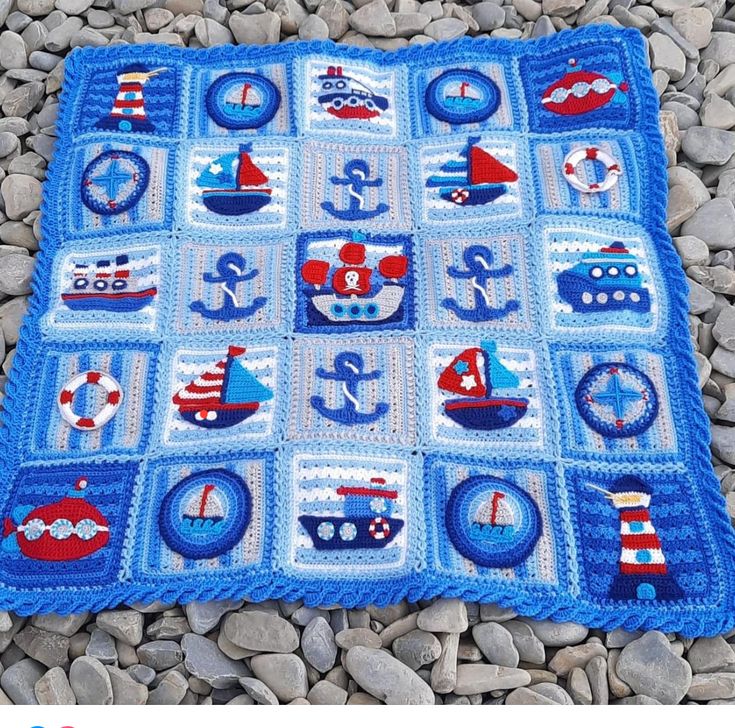 a blue crocheted blanket with boats and ships on it, sitting on some rocks