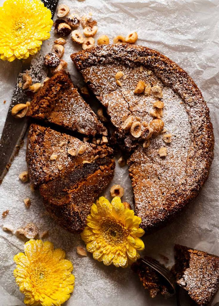 a piece of cake with nuts and flowers on the side, next to a knife