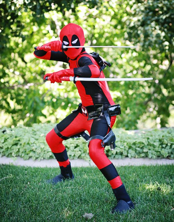 a man in a red and black costume is holding two swords while standing on the grass