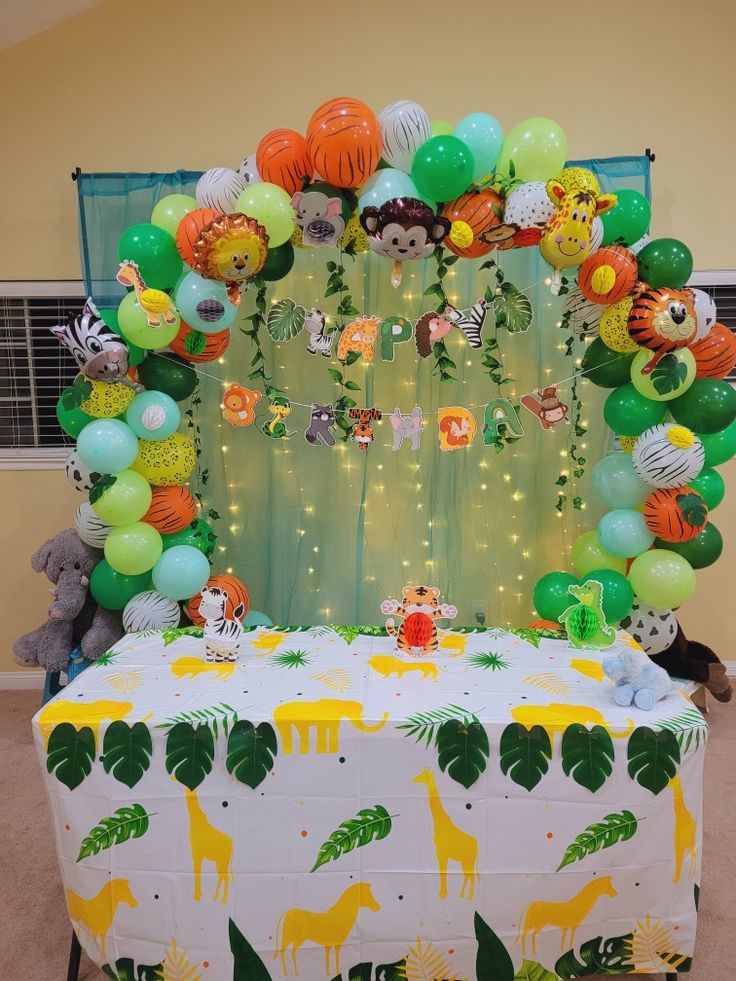 an animal themed birthday party with balloons and jungle animals on the back of a table