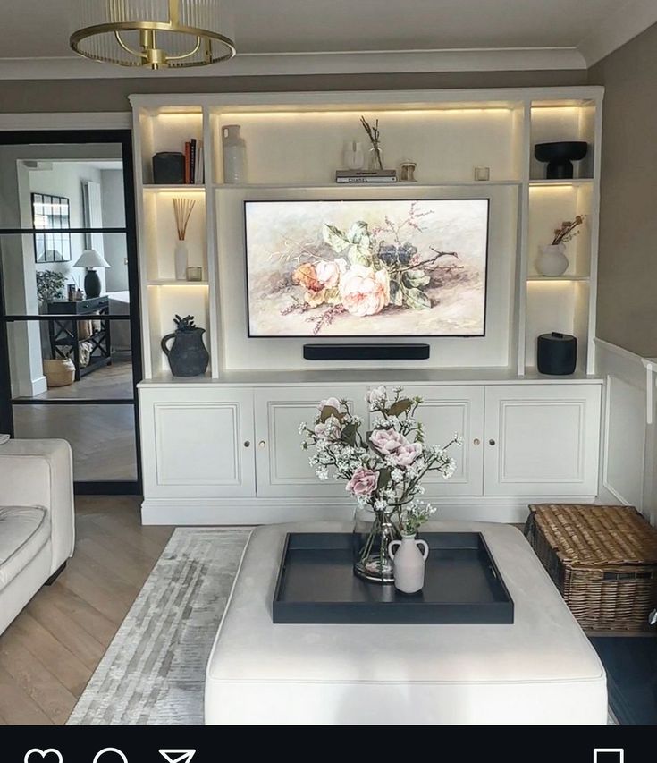 a living room with white furniture and a flat screen tv mounted on the wall above it