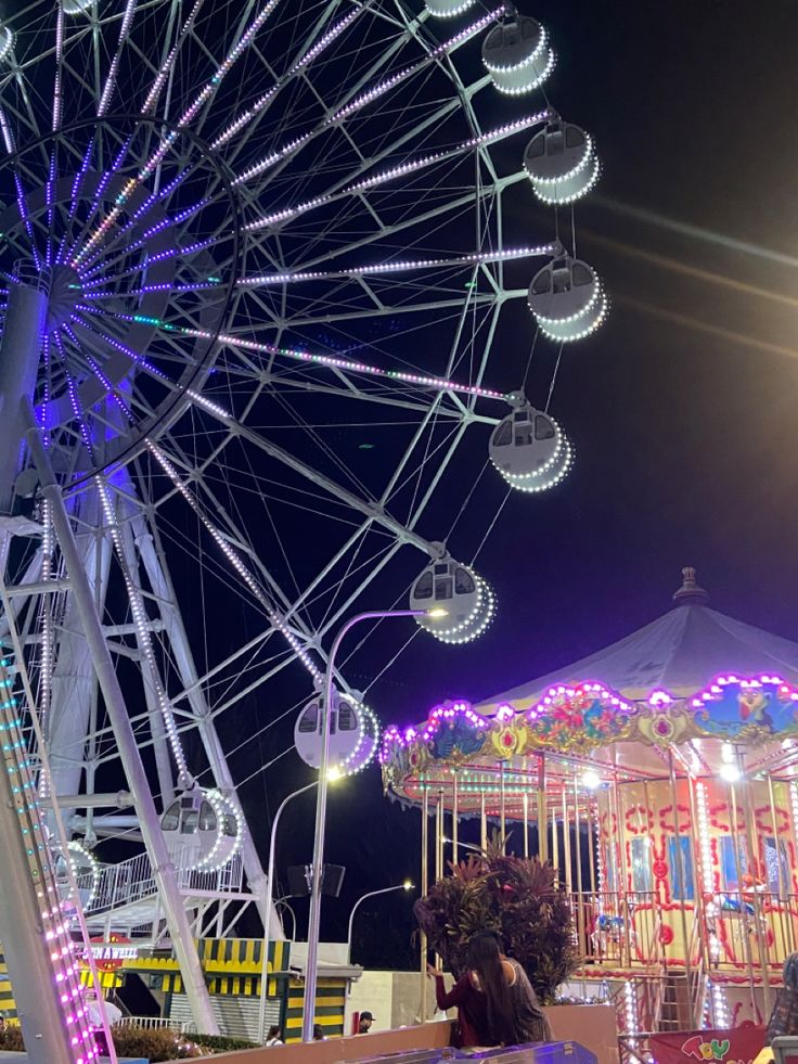 the ferris wheel is lit up at night with colorful lights on it's sides