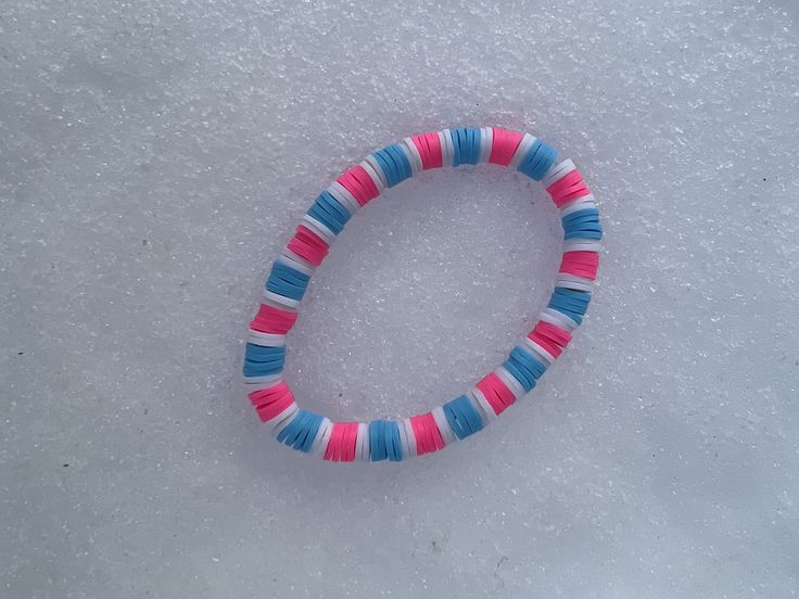 a pink, blue and white beaded bracelet laying on top of snow covered ground