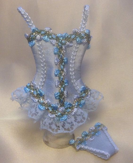 a white corset with blue beads and lace on the bottom is next to a pair of slippers