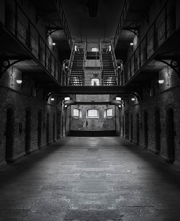 black and white photograph of the inside of a jail cell building with graffiti written on it