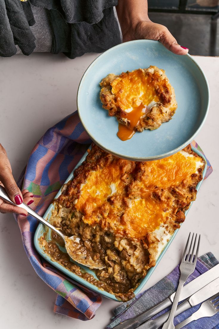 a person is holding a fork and spoon over a plate with a casserole on it