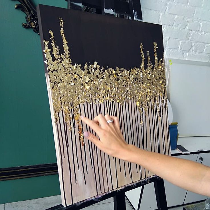 a woman is painting gold leaf designs on a black and white canvas with her finger