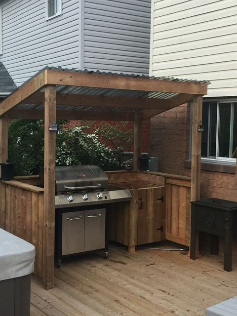 an outdoor kitchen with grill and bbq in the back yard on a wooden deck