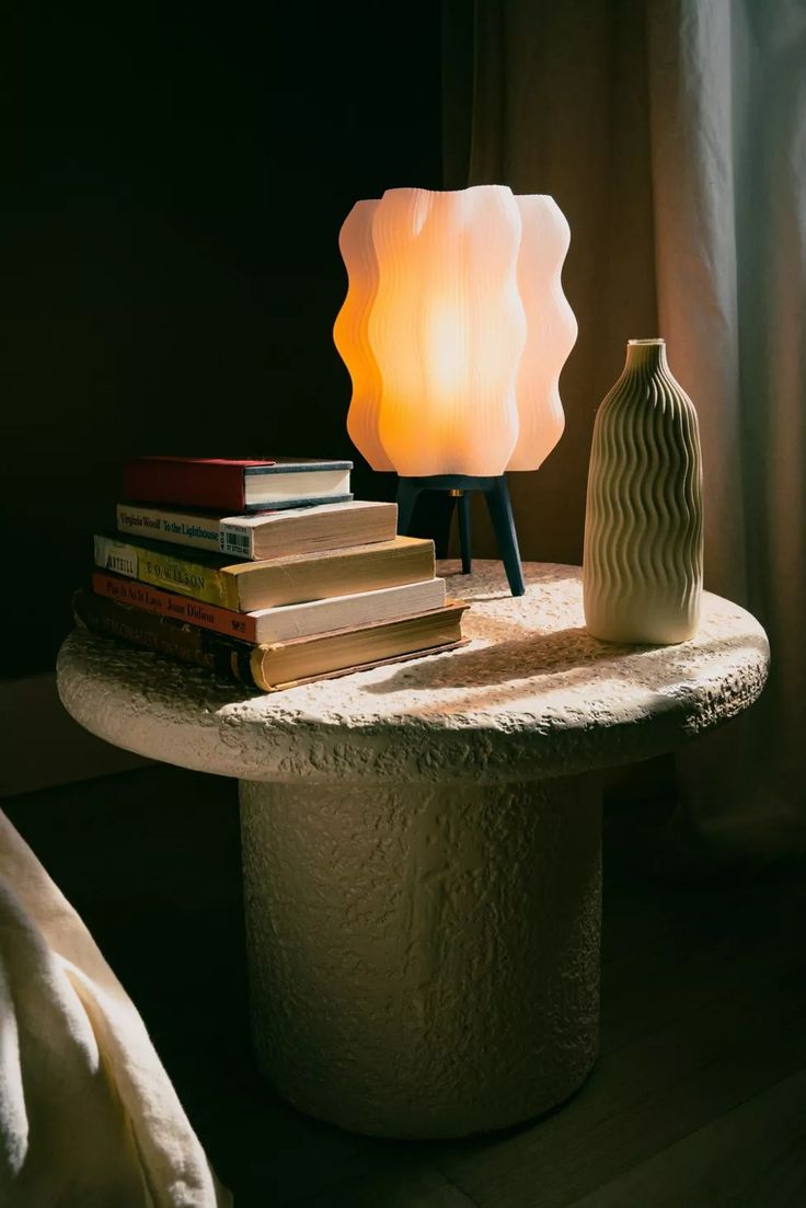 a lamp sitting on top of a table next to a stack of books and a vase