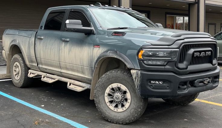 a large gray truck parked in a parking lot next to a building with two cars