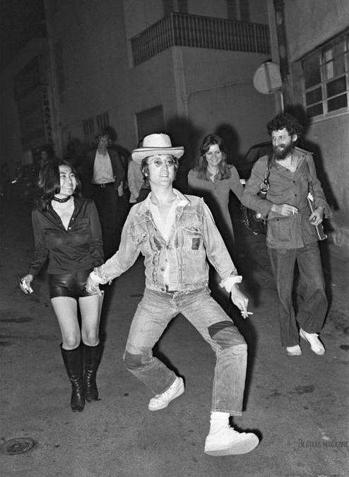 a group of people dancing in the street at night with one person wearing a cowboy hat