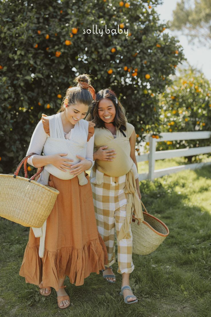 two pregnant women standing next to each other in front of an orange tree and holding baskets