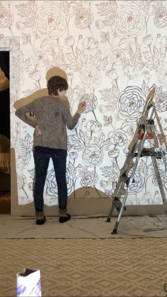 a man standing in front of a wall with flowers on it and painting the walls