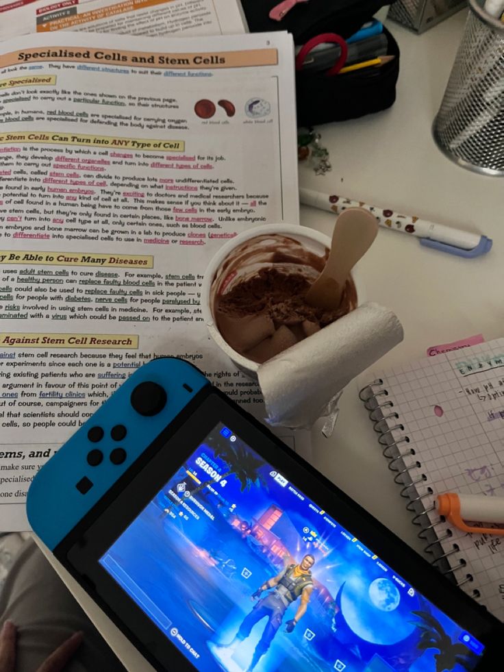 a person holding a nintendo wii game controller next to a cup of coffee and an open book