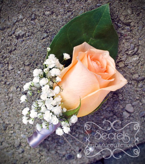 an orange rose and white baby's breath boutonniere on the ground