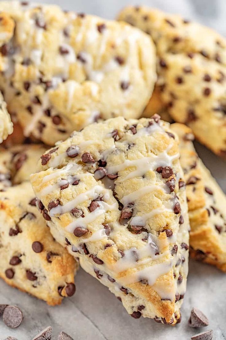 chocolate chip scones with white icing and chocolate chips on the side, sitting on a piece of parchment paper