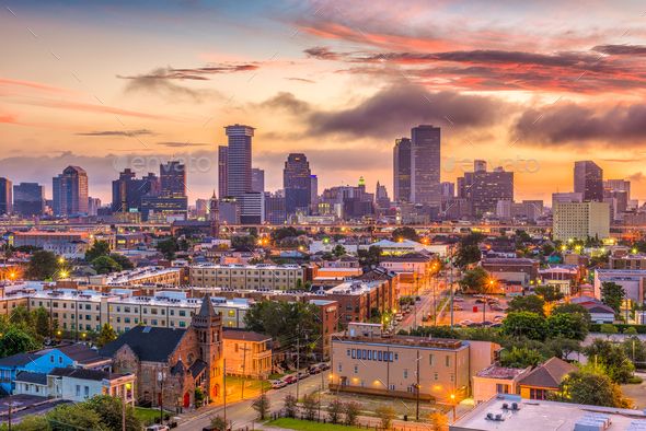 the city skyline is lit up at sunset with clouds in the sky and buildings on either side