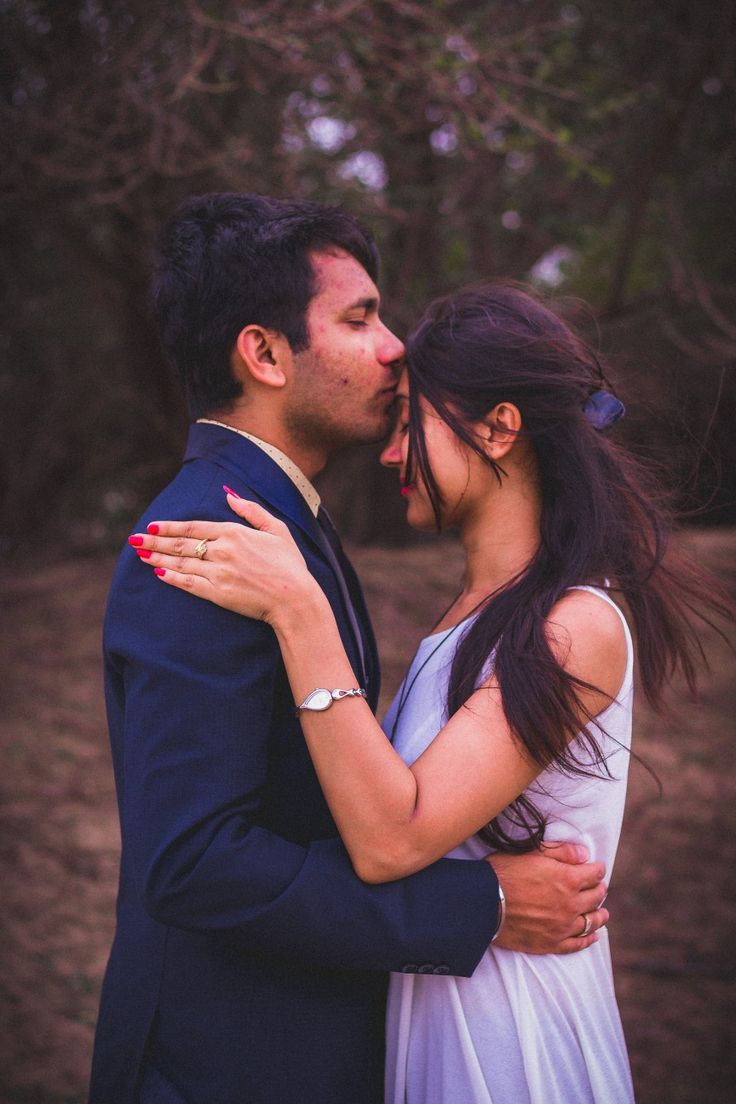 a man and woman kissing each other in the middle of an outdoor area with trees behind them