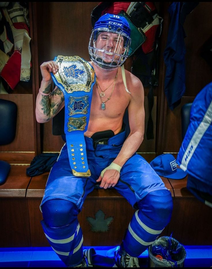 a man sitting on top of a bench wearing blue pants and holding a wrestling belt